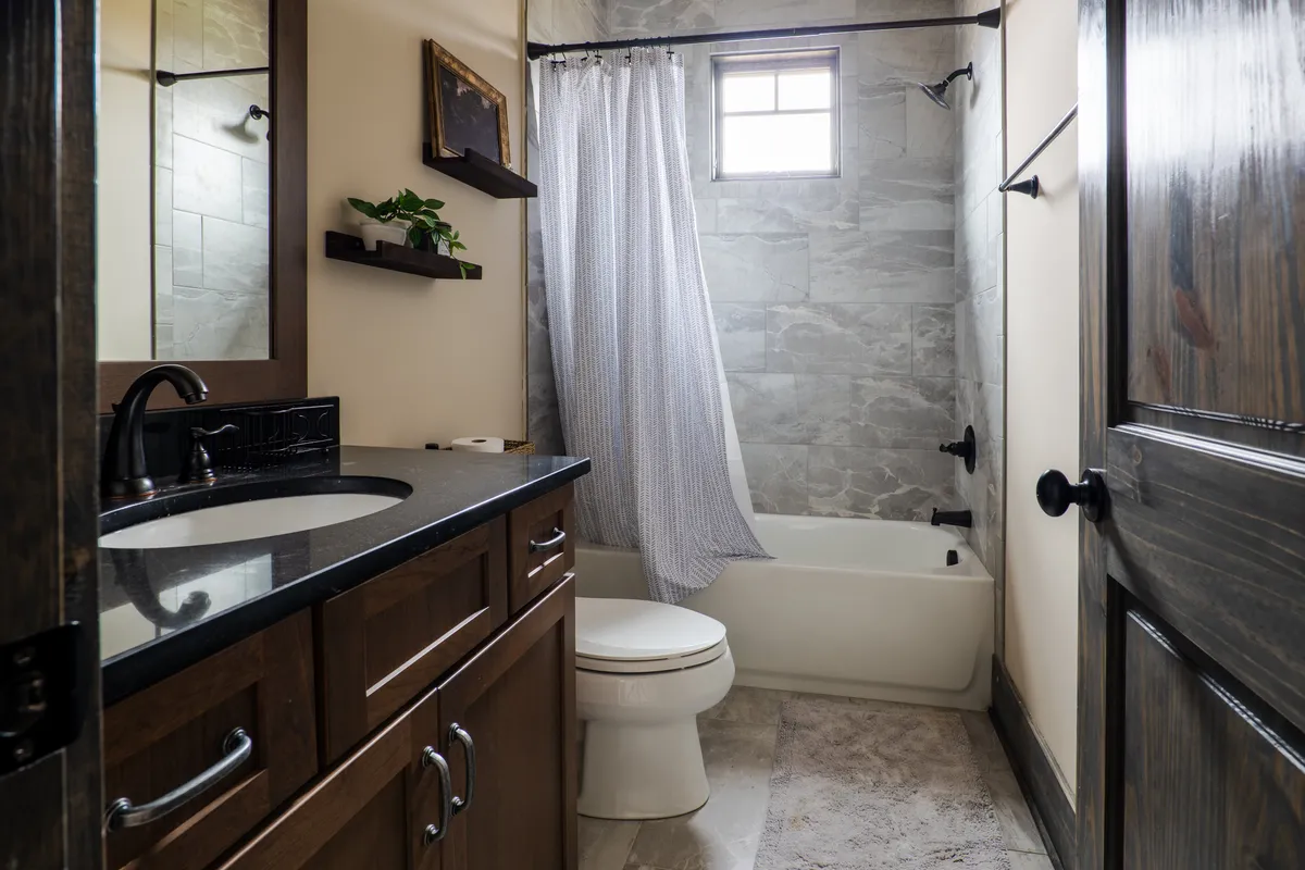 A modern bathroom with a full-size tub, dark wood cabinetry, a shower area with curtain, and small window. The space is inviting and practical, ideal for post-adventure clean-ups.