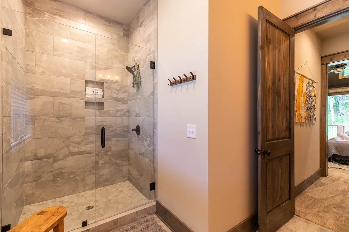 A close-up of a glass shower enclosure with textured tile walls and a wooden bench, creating a tranquil, rejuvenating space ideal for relaxing and refreshing after a day of adventure.