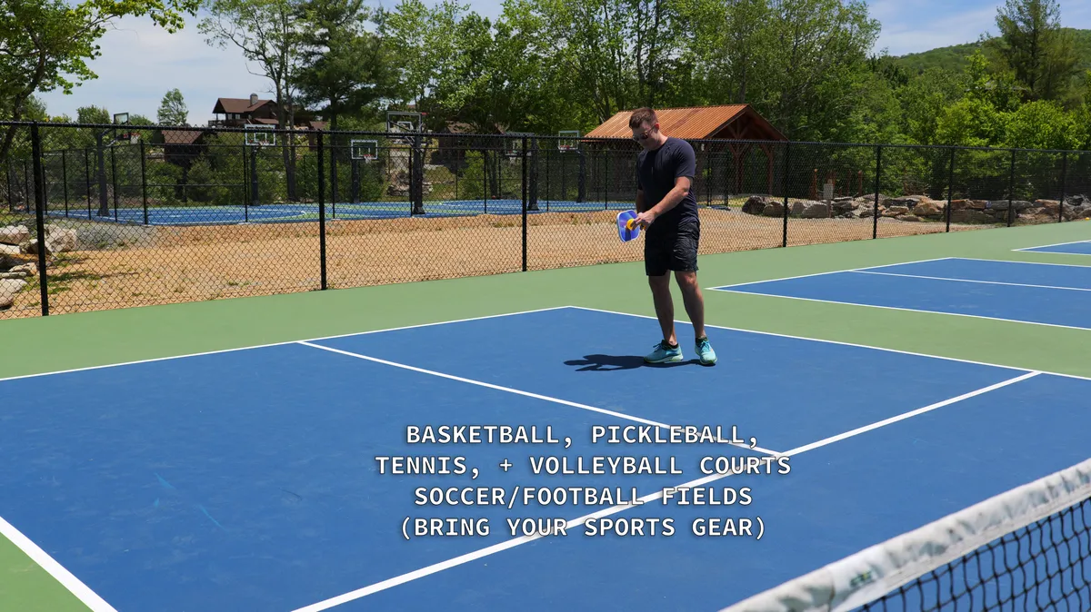 A lively sports court set amidst greenery, with someone playing and ample space for basketball, pickleball, tennis, or volleyball. The scene conveys energy, activity, and group fun within a vibrant outdoor environment.
